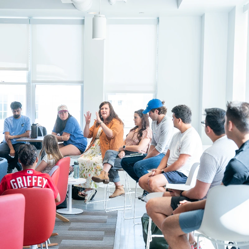 Woman leading a vibrant group discussion with diverse young adults in a bright, modern workshop setting.