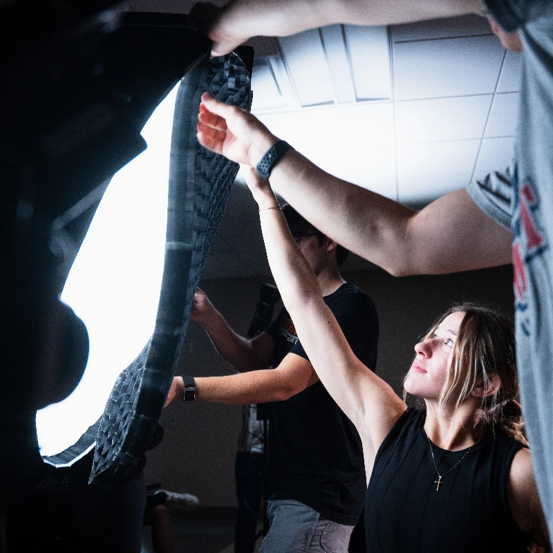 A production team collaboratively adjusting a large softbox light with a grid for a photo or video shoot.
