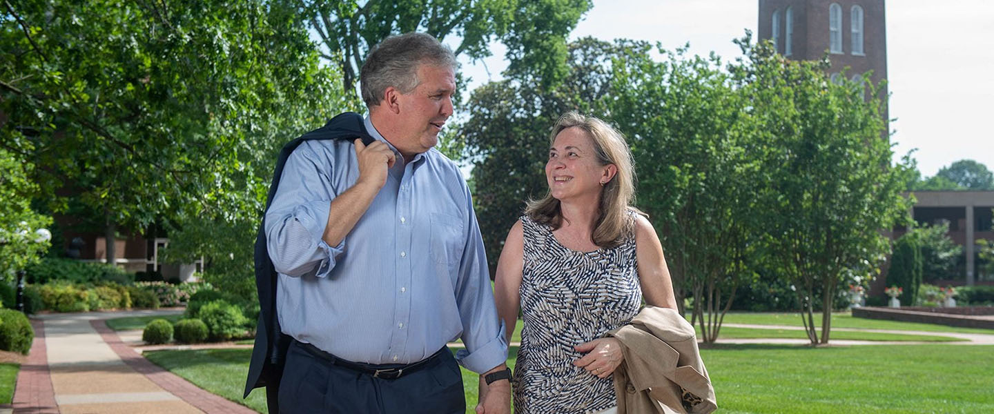 Greg and Susan Jones walking through campus with the bell tower in the background