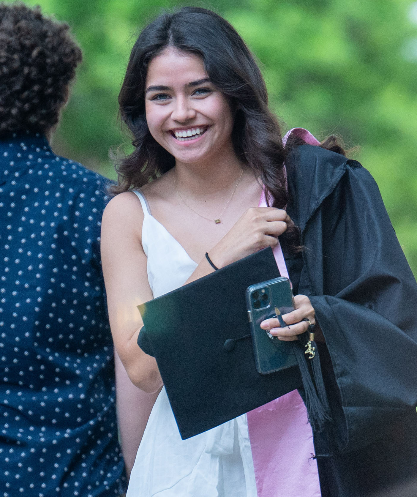 A graduating student walks down a walkway with a warm smile on her face
