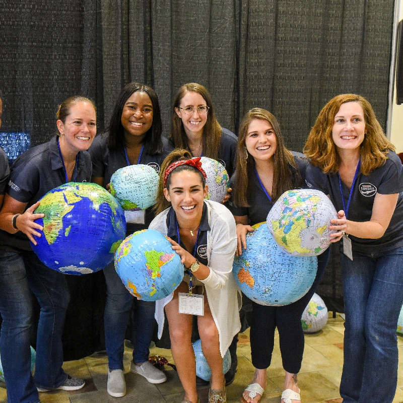 Seven smiling women holding inflatable globes, representing global connection and diversity at an event.