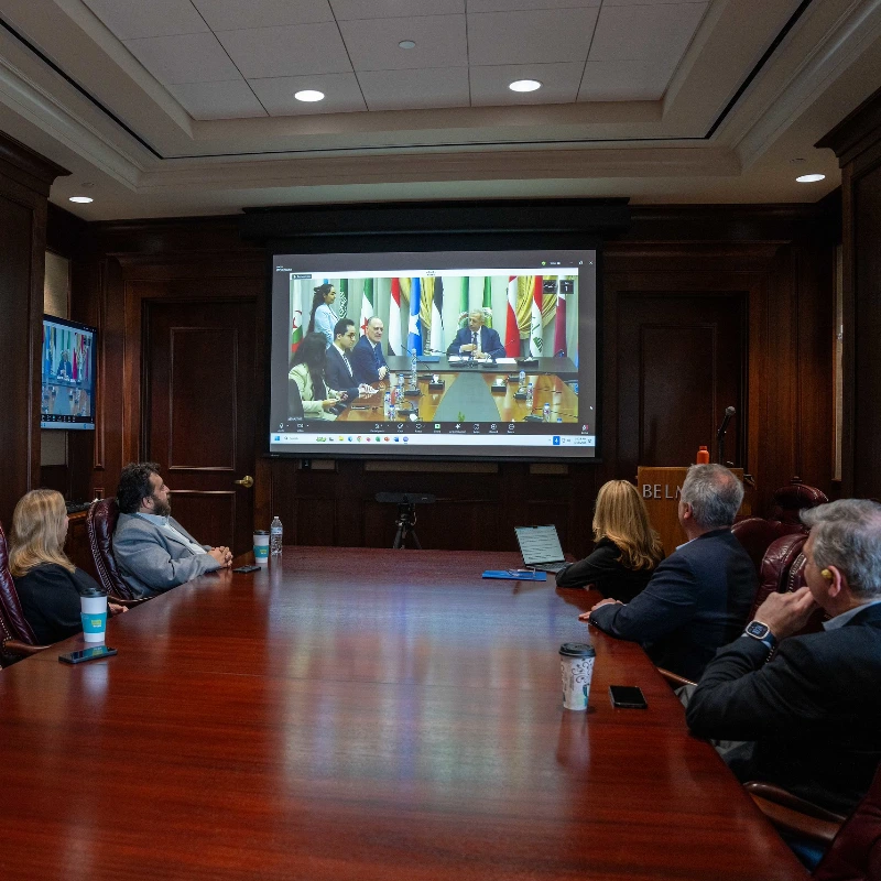 People in a conference room watching an international video conference on a large screen.