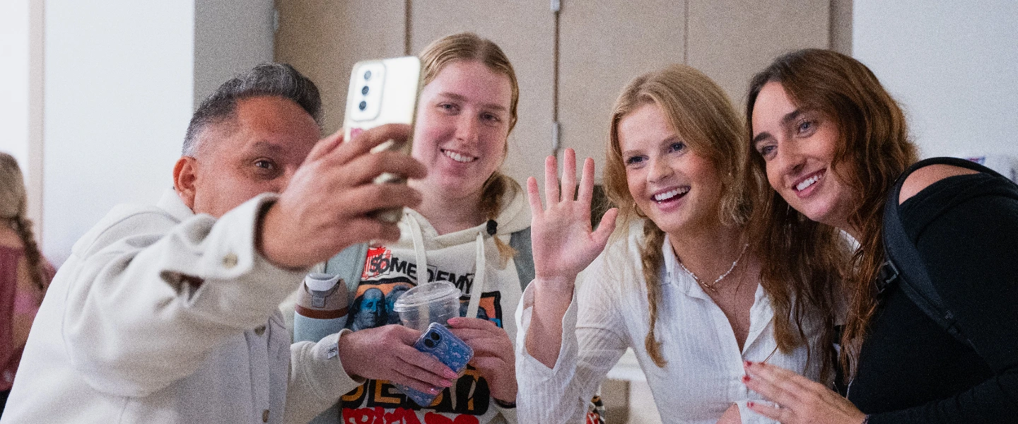 Group of people taking a selfie, smiling and waving happily for the camera.