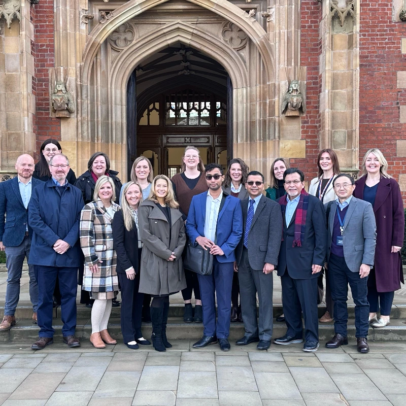 Diverse group of professionals and academics pose in front of a historic university building entrance.