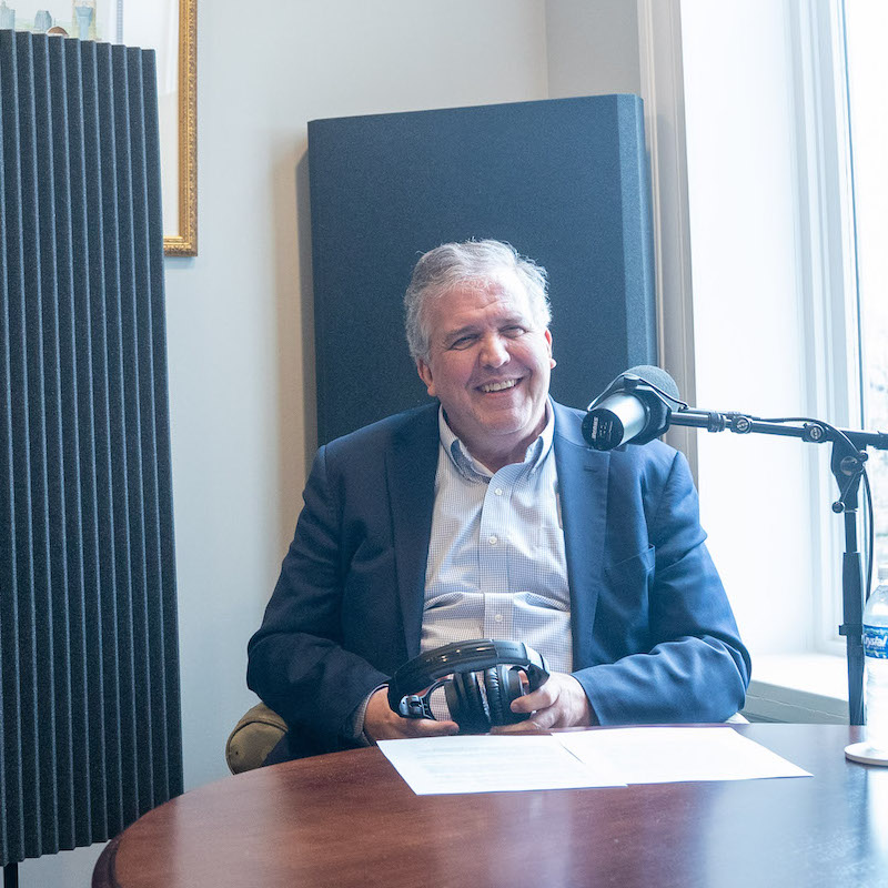 Dr. Greg Jones smiling as he sits in front of a microphone with headphones in hand