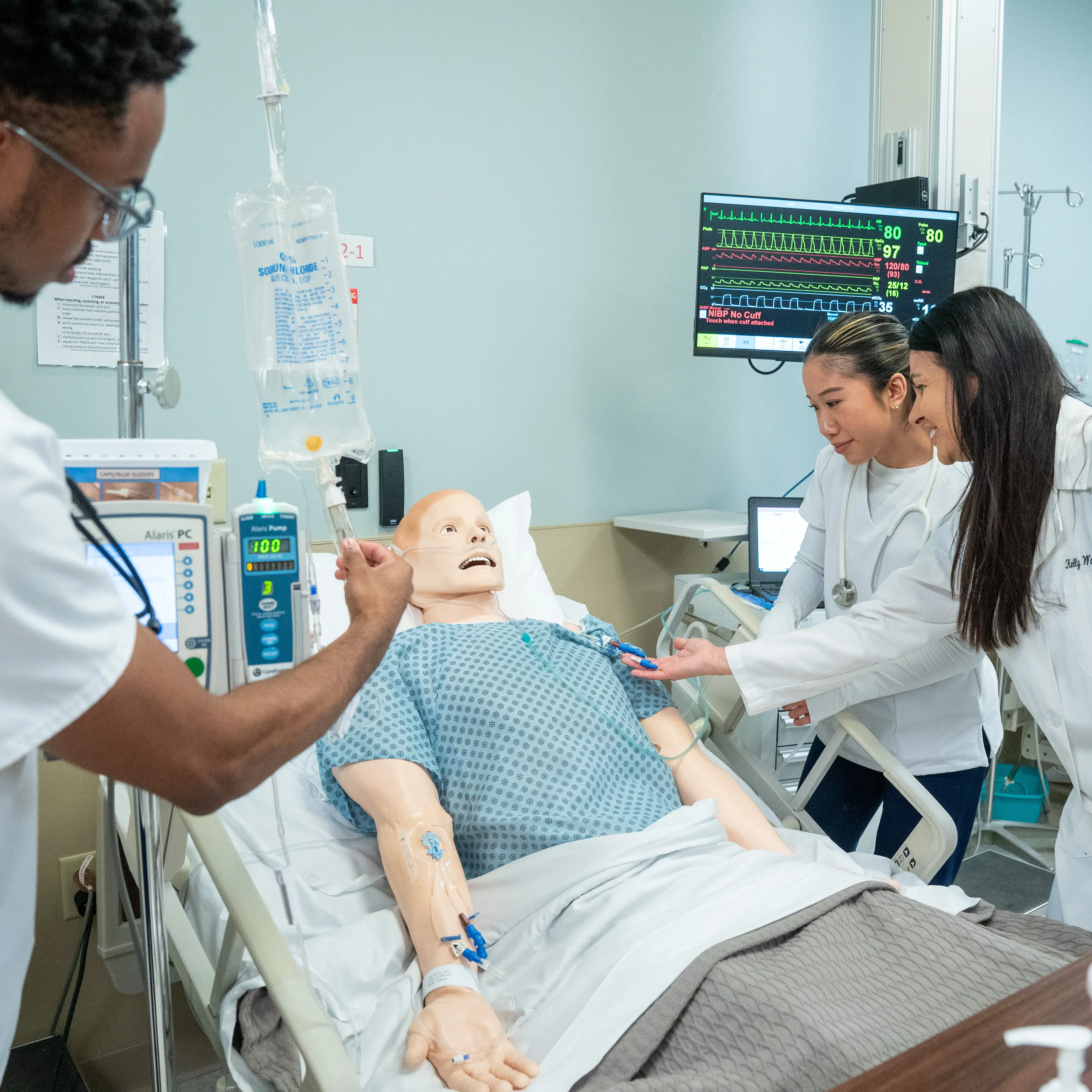 Nursing students and a clinical instructor review patient procedures together in a hospital-style simulation room at Belmont University.