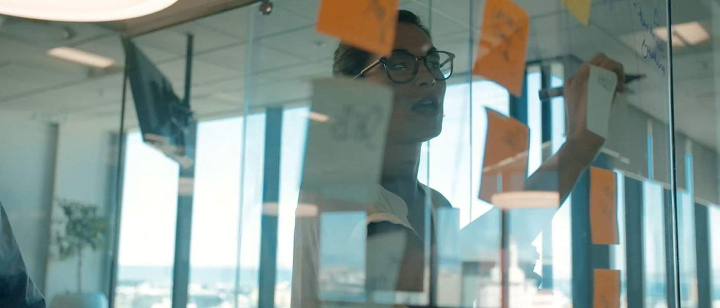A woman writing on glass that is covered in sticky notes