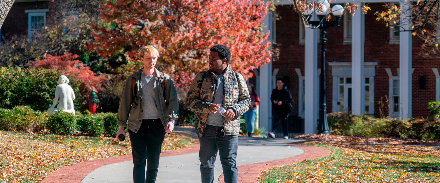 2 students talking and walking outside on the historic side of campus on a sunny fall day