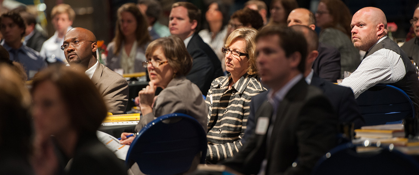 Workshop attendees listen to presenter while seated at a table.