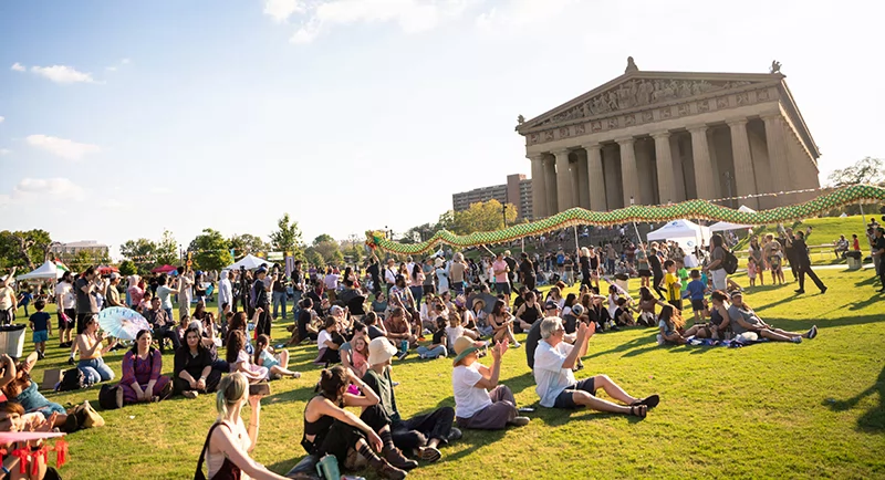 Crowd gathered on the lawn in front of Nashville’s Parthenon on a sunny day, with people sitting, walking, and enjoying a festival.