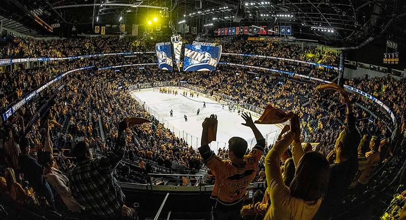 Packed arena of Nashville Predators fans cheering as players gather on the ice under a scoreboard that reads “WIN.”
