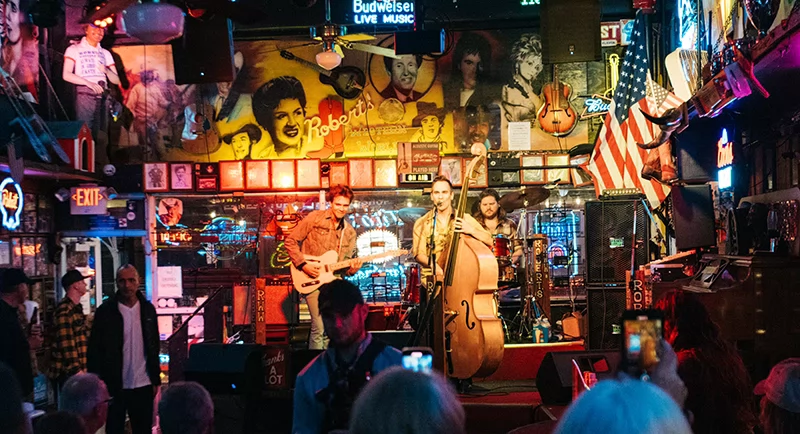 Band performing onstage at Robert’s Western World with guitar, upright bass, and drums as a crowd watches inside the neon-lit honky-tonk.