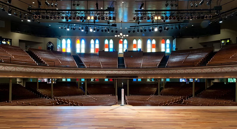 View from the Ryman Auditorium stage looking out at empty wooden pews and colorful stained-glass windows.