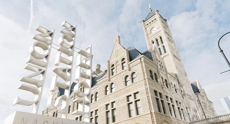 The historic Union Station Hotel in Nashville with its stone architecture and tall clock tower beside a modern white sign.