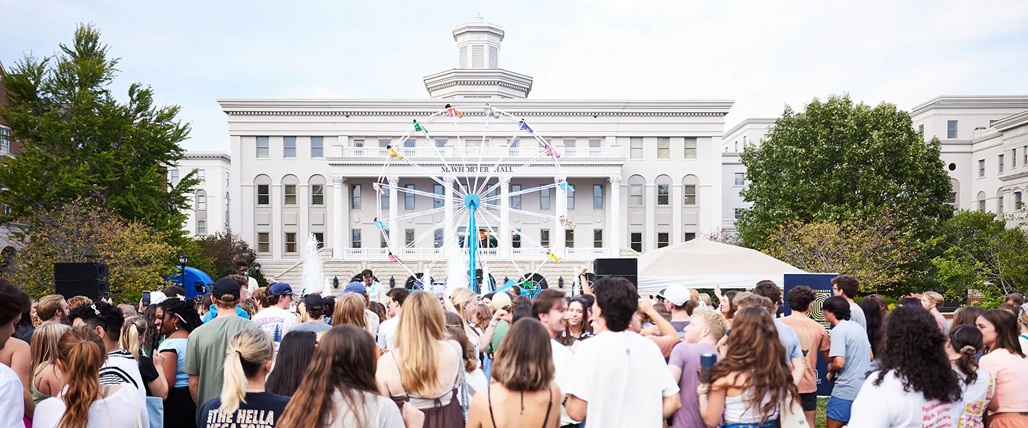 A large crowd gathers in front of McWhorter Hall at Belmont University, with a Ferris wheel set up for a campus event.