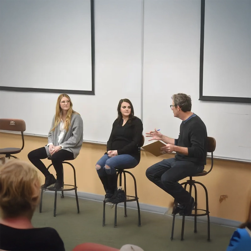 Megan Feeman, co-founder of No Baked Cookie Dough, sits on a panel with another speaker and a moderator in a classroom setting, discussing entrepreneurship and sharing insights with the audience.