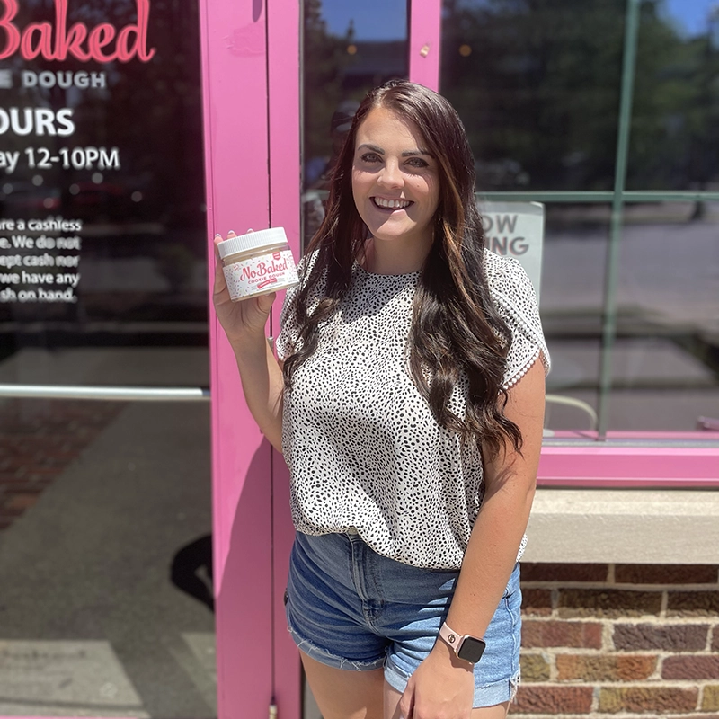 Megan Feeman, standing in front of NoBaked cookie dough store holding a cup of NoBaked cookie dough