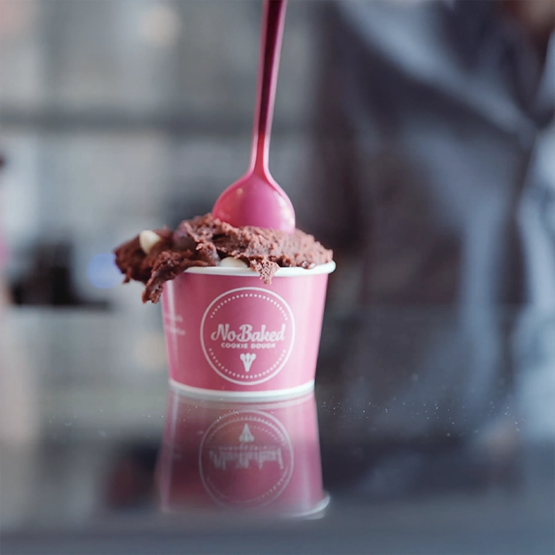 An image of a cup of NoBaked cookie dough with a pink spoon in the cup