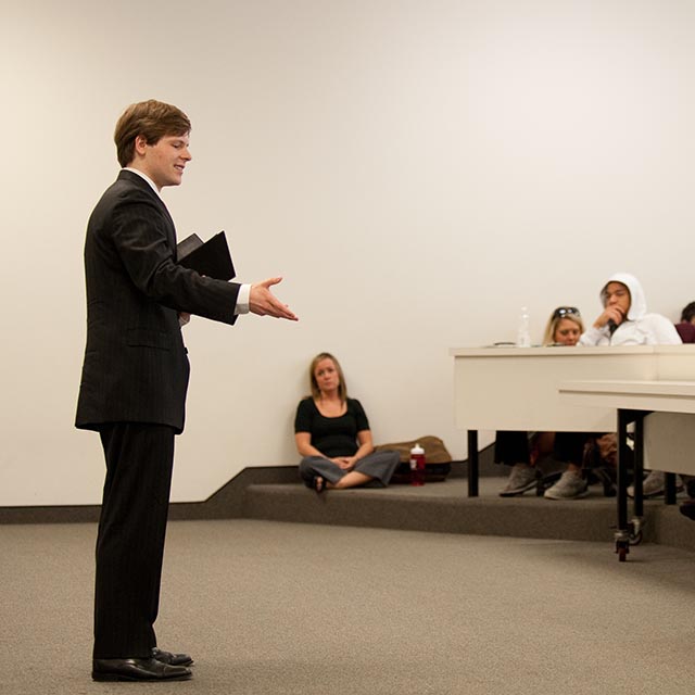 Student presenting debate topic in suit and tie