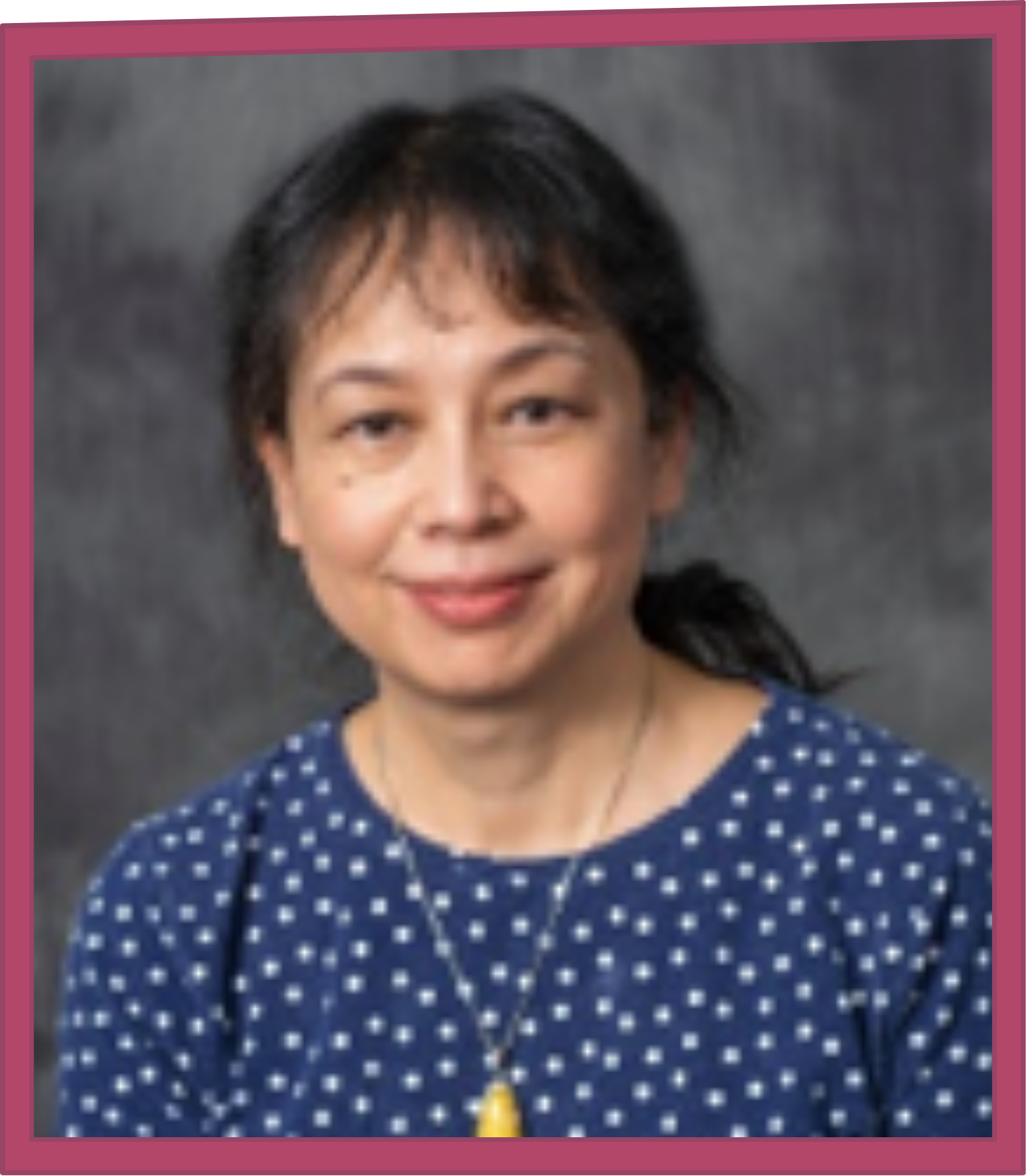 Head-and-shoulders portrait of a smiling woman in a blue polka-dot top, against a gray studio background.