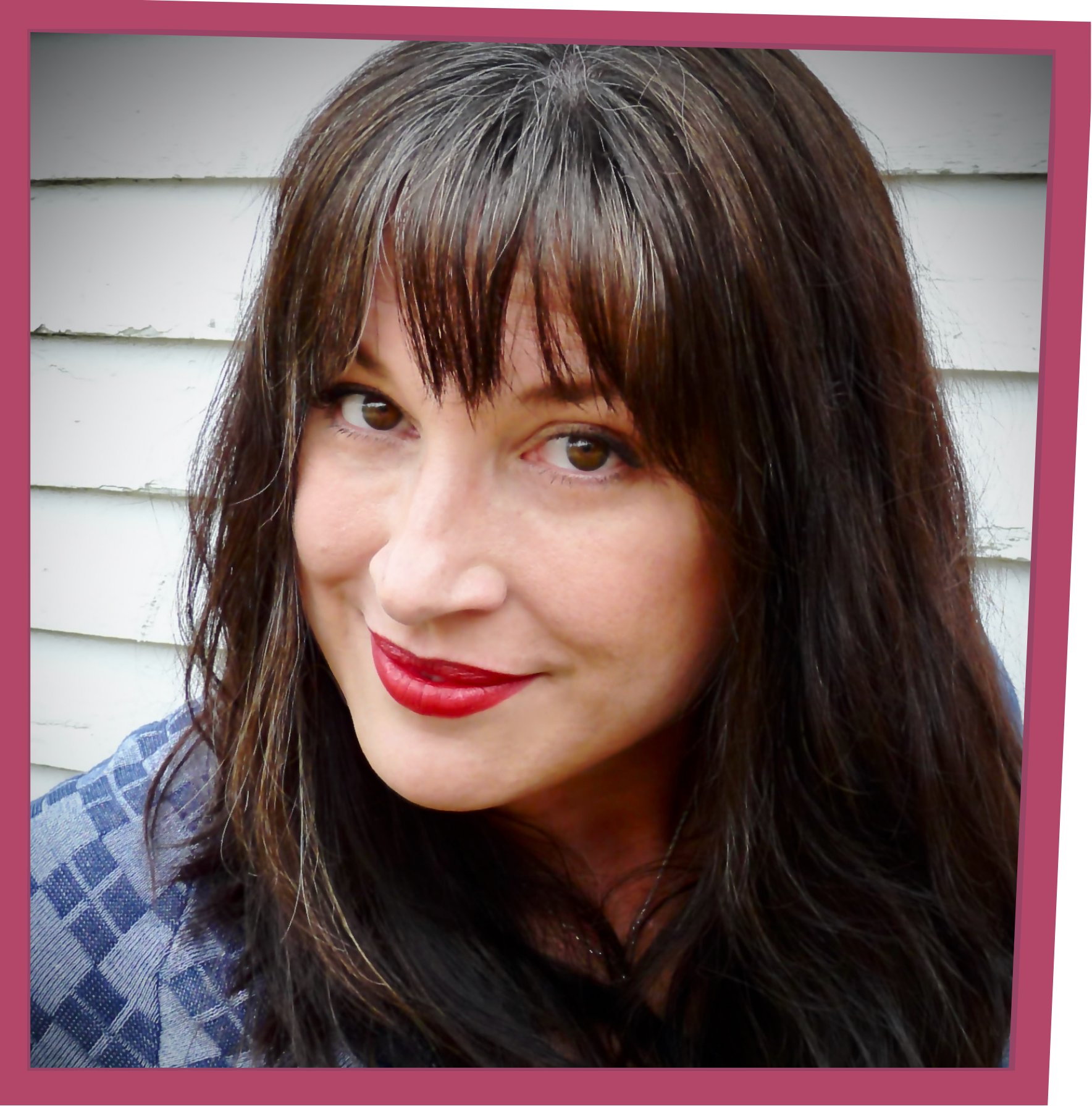 Close-up portrait of a woman with long dark hair and bangs, wearing red lipstick and looking upward against a white siding background.