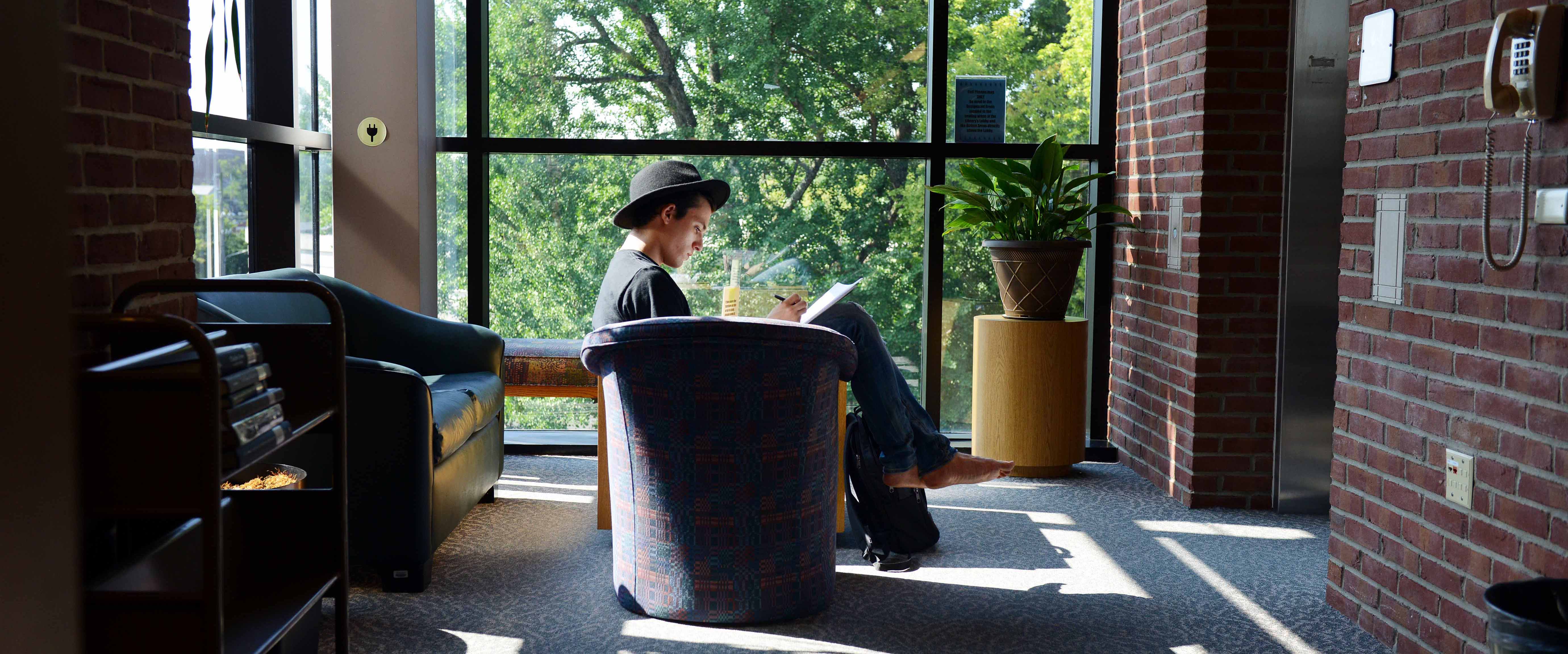 Student sitting in chair by window with a book in the library