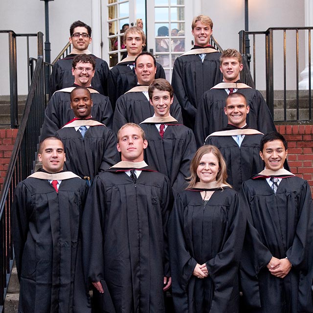 Graduate MBA students posing on a stair case in their gowns and hoods