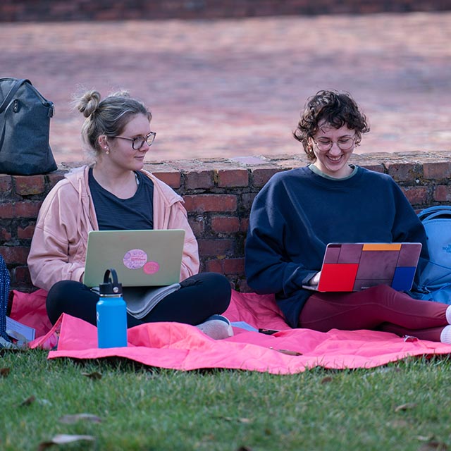 students talking to each other on lawn while on their laptops
