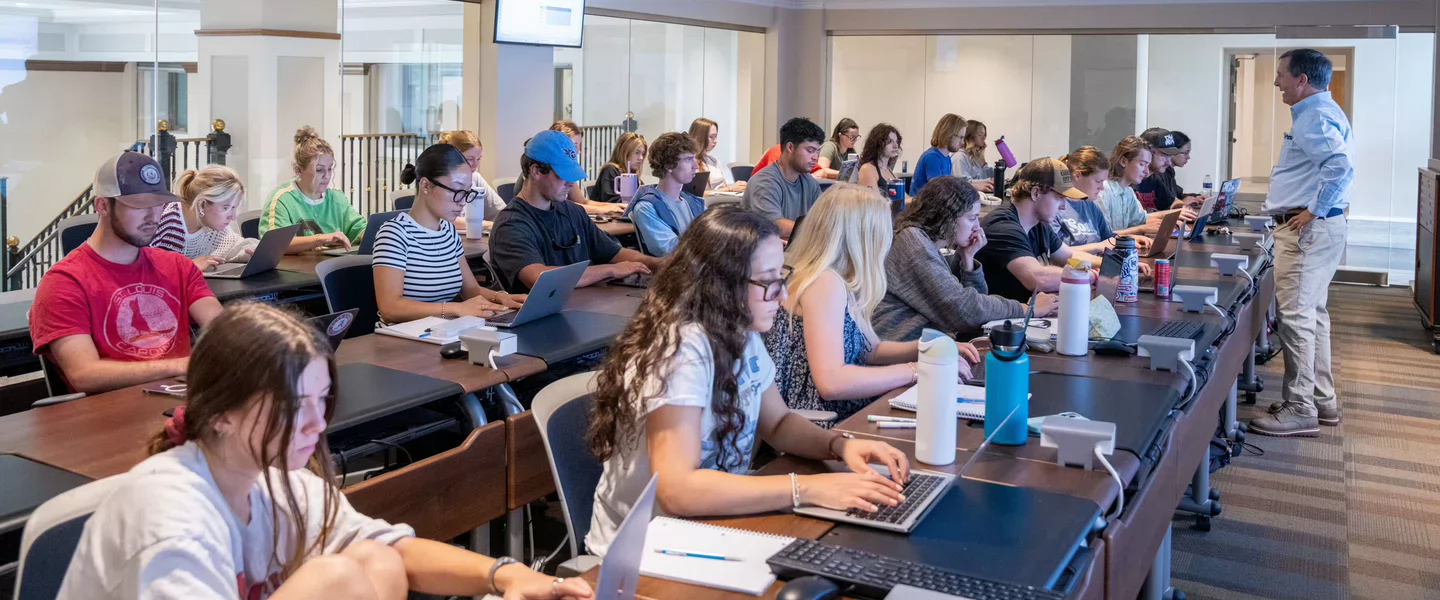 Classroom full of students sittling at tables listening to a professor talk