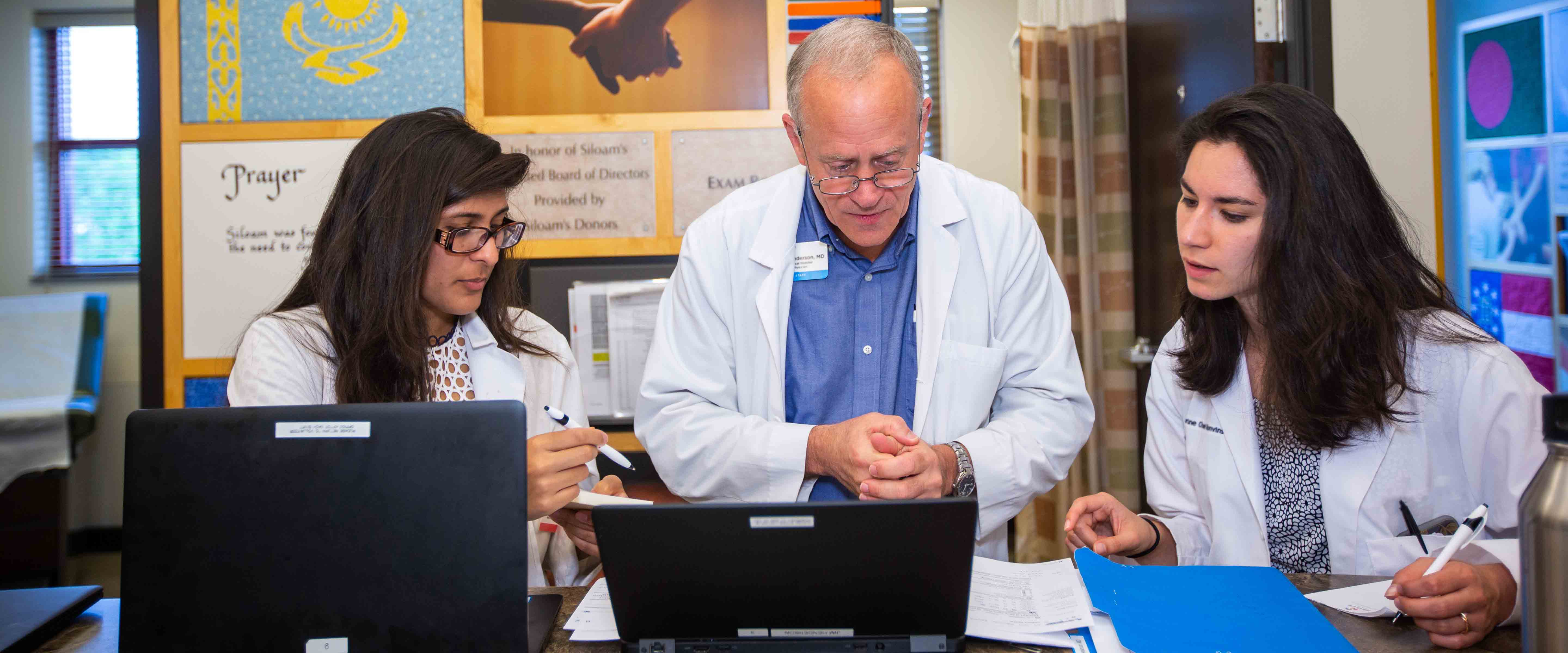 Resident Doctor teaching 2 medical school students about charting on a computer