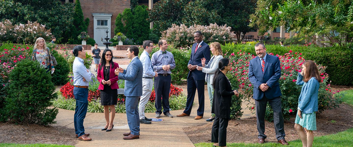 Medical school employees talk outside in front of the bell tower while waiting to take groups photos