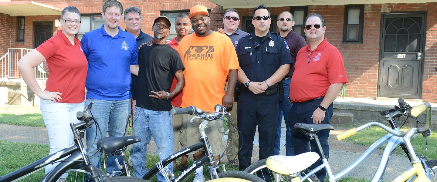 Community volunteers and police with new bicycles in front of homes, promoting neighborhood safety.