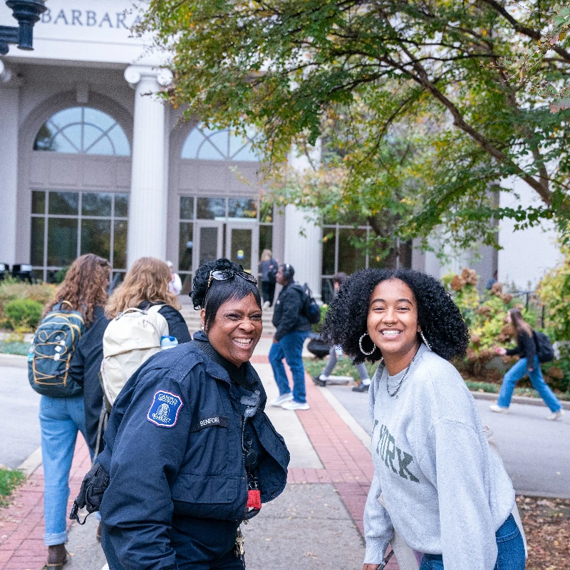 Smiling security officer and student in "New York" shirt on a college campus.