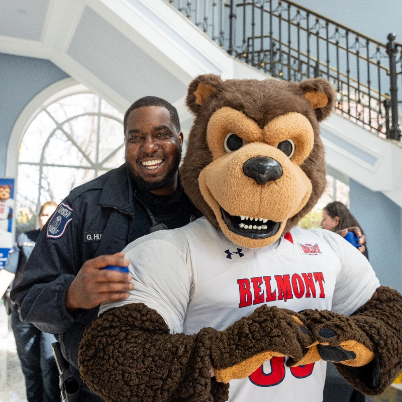 Smiling security officer with Belmont University's bear mascot, wearing a 'Belmont' shirt.