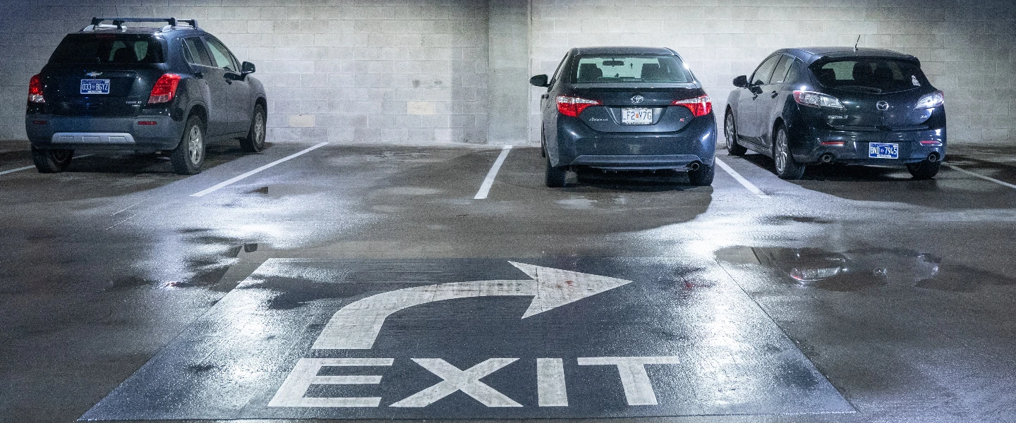 Wet parking garage floor with a white 'EXIT' sign and arrow, and three cars parked.