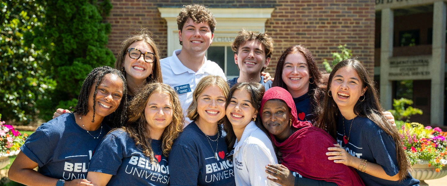 Diverse group of smiling Belmont University students, many wearing school shirts, on campus in front of a brick building.