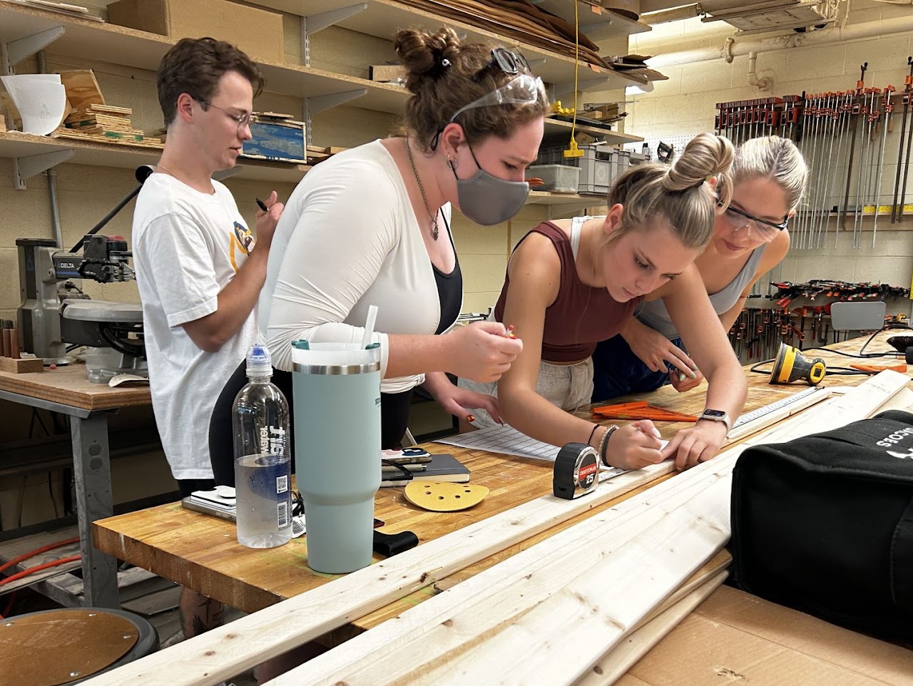 A small team of workers leaning over a table and measuring  planks of wood