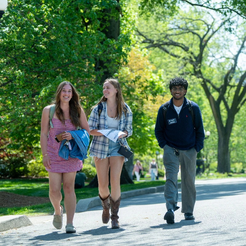 Three Belmont University students walk and smile together on a tree-lined campus path on a sunny day.Three Belmont University students walk and smile together on a tree-lined campus path on a sunny day.