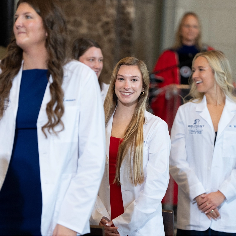 Smiling healthcare students in white lab coats at a Belmont University white coat ceremony.