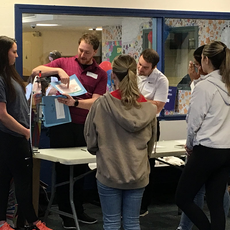 man pointing to booklet he is holding up to show the group of students how to do an activity