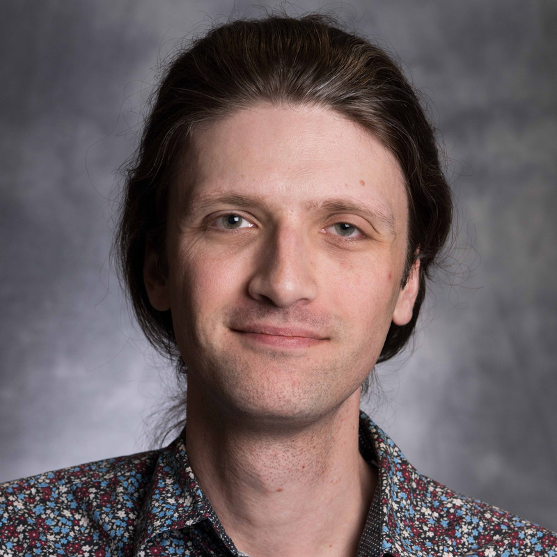 Headshot for Sam Phillips, a lean, white man with dark hair