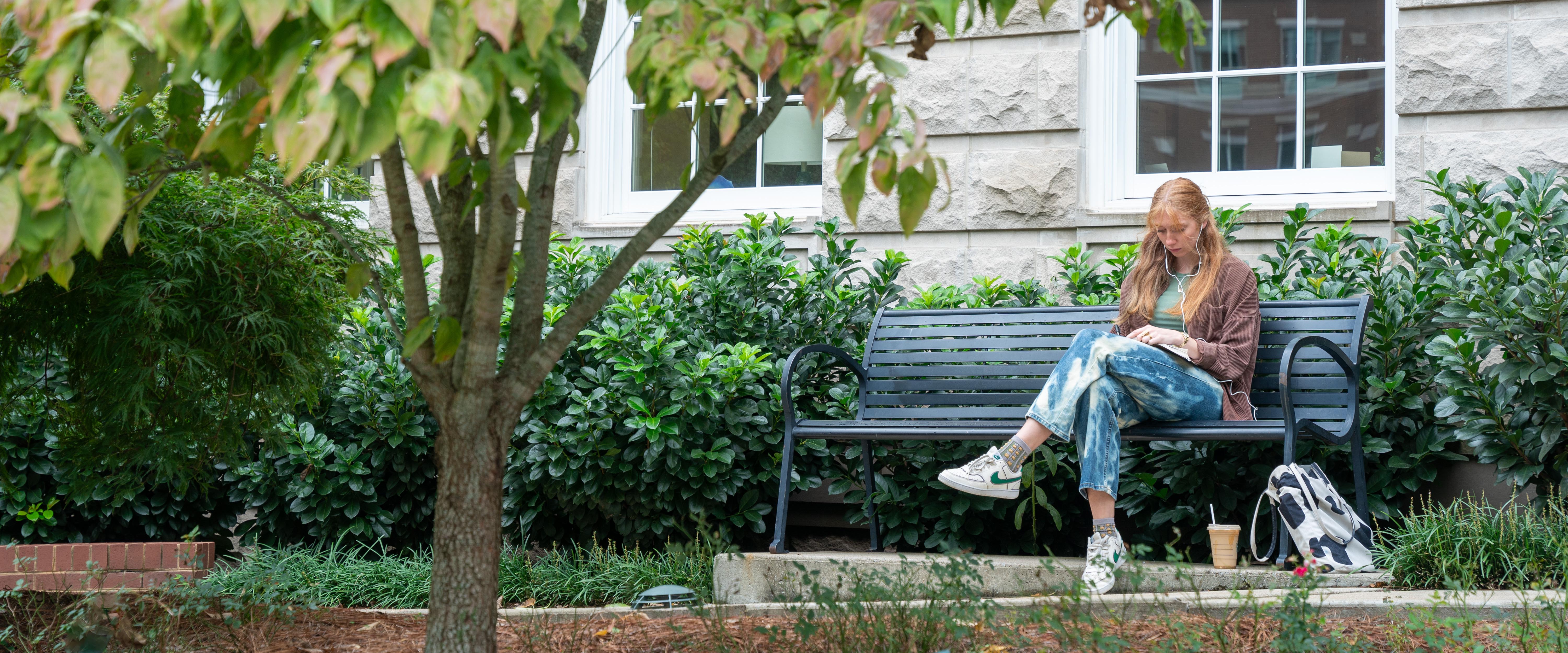 Student sitting on a bench listening to music while reading a book