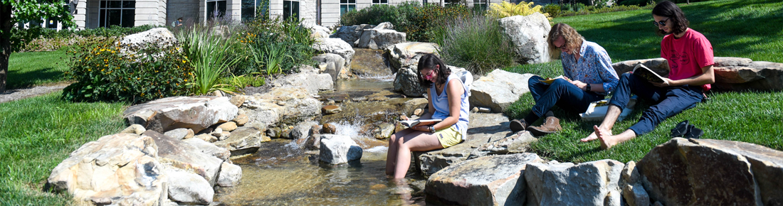 A photo of Belmont students reading books while sitting near Bear Creek outside of Tall Hall.