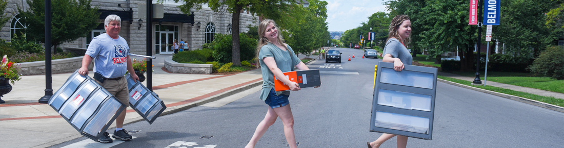 A photo of a Belmont student and her parent carrying storage bins across a street.