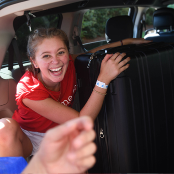 A photo of a female Belmont student picking up a suitcase from the rear of a vehicle.