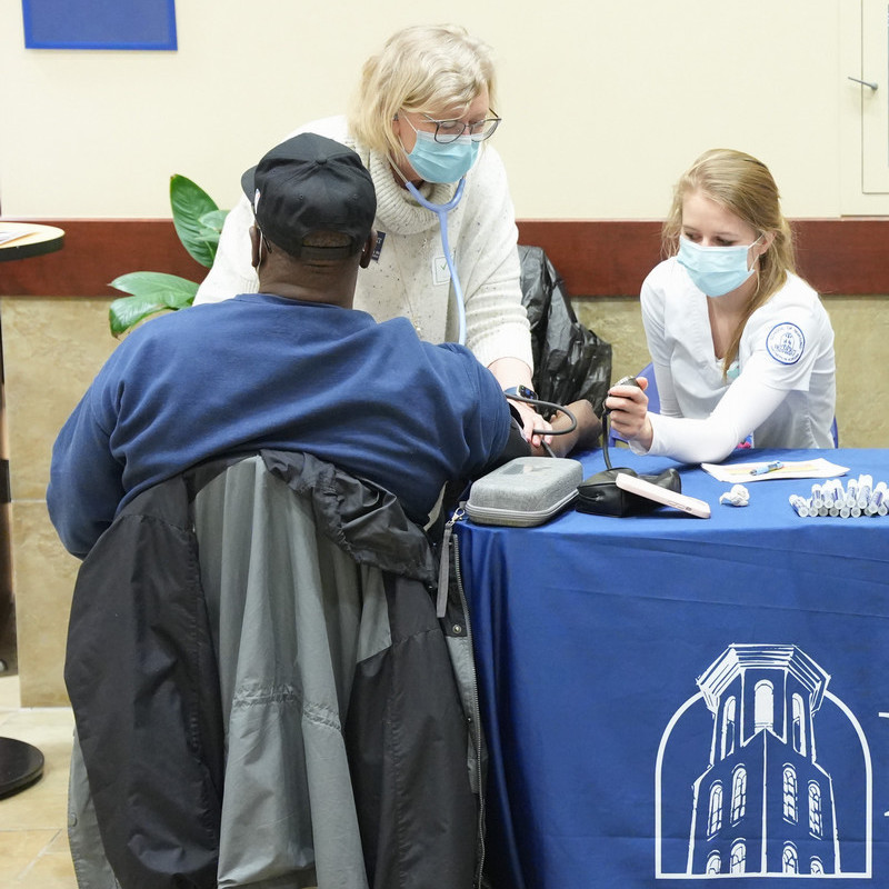 Professor assisting a nursing student in taking the blood pressure of a man