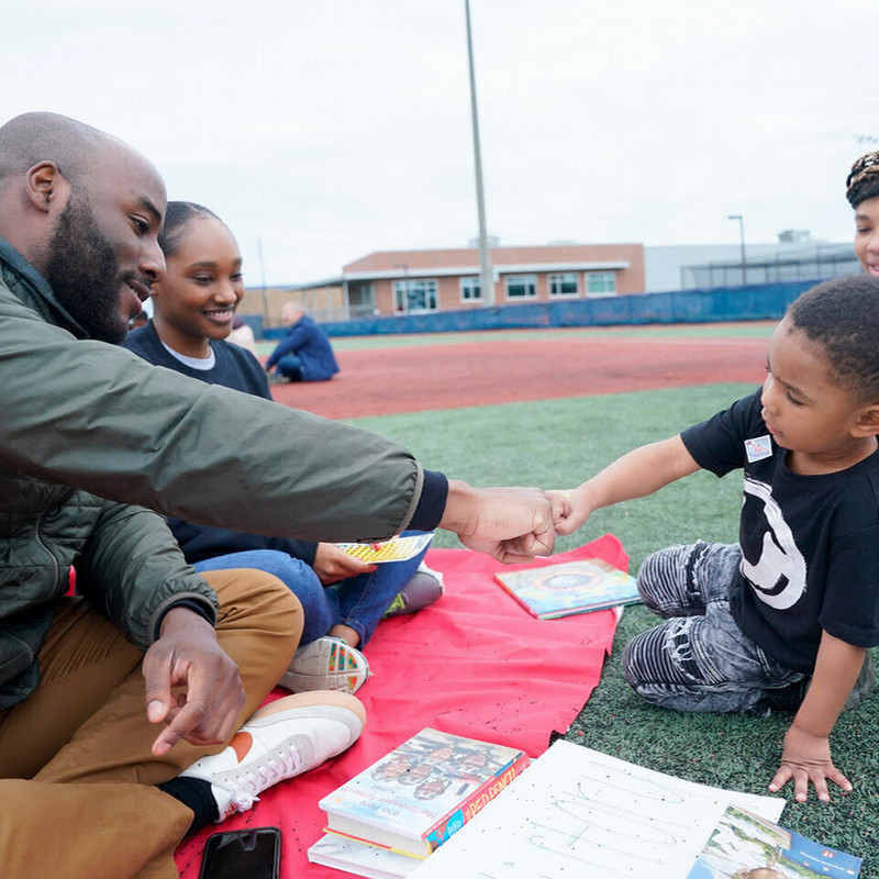 a student gives a young child a fist bump while sitting on the grass