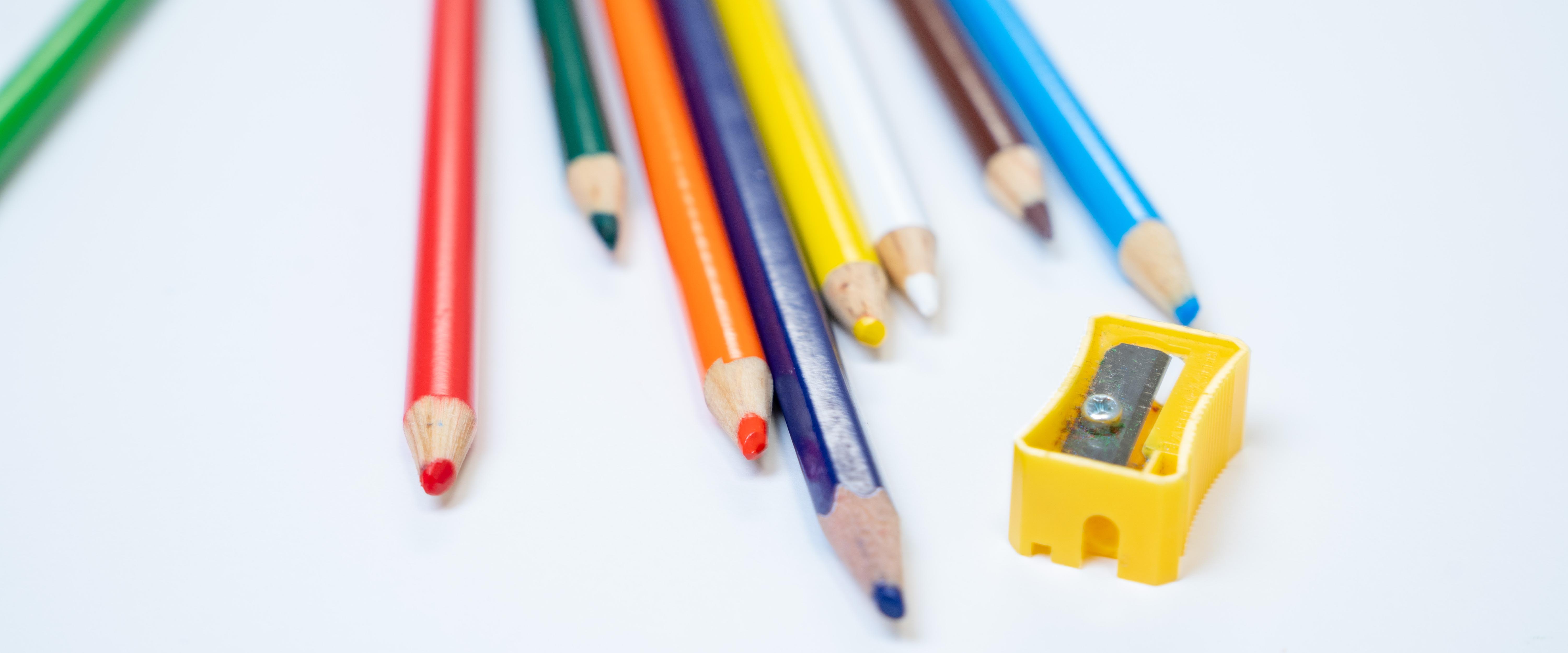 Close up of colored pencils and a pencil sharpener on a white background