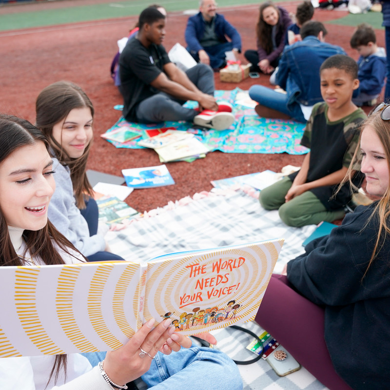 Belmont Students reading to elementary students outside on a field