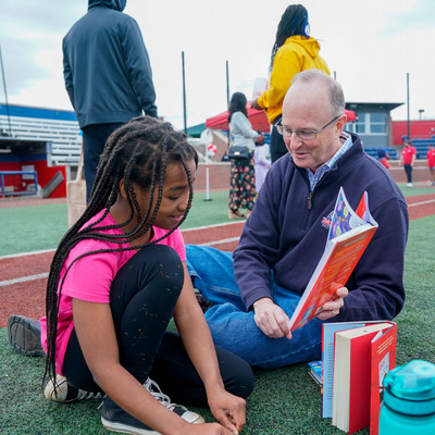 Belmont employee reading to a child while sitting in the grass outside